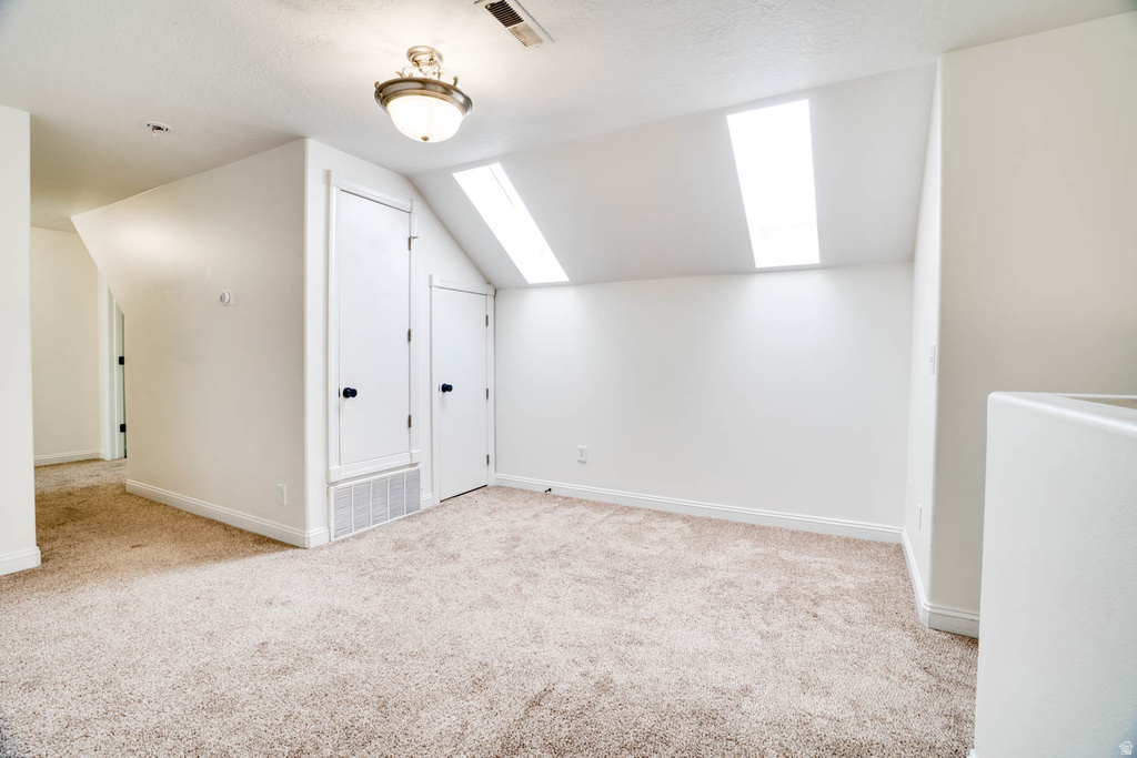 Carpeted room featuring two skylights, white walls, and a ceiling-mounted light fixture