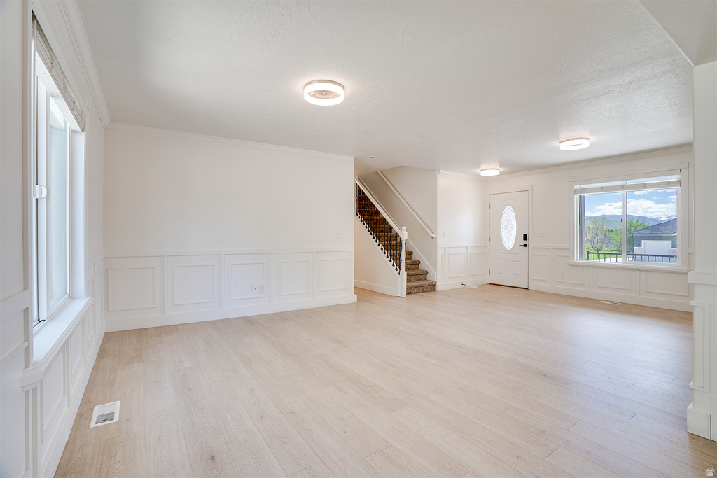 Expansive open-concept room featuring light wood-finish flooring, wainscoting paneling, recessed lighting, a front entry door with an oval glass insert, and a staircase with wrought iron balusters