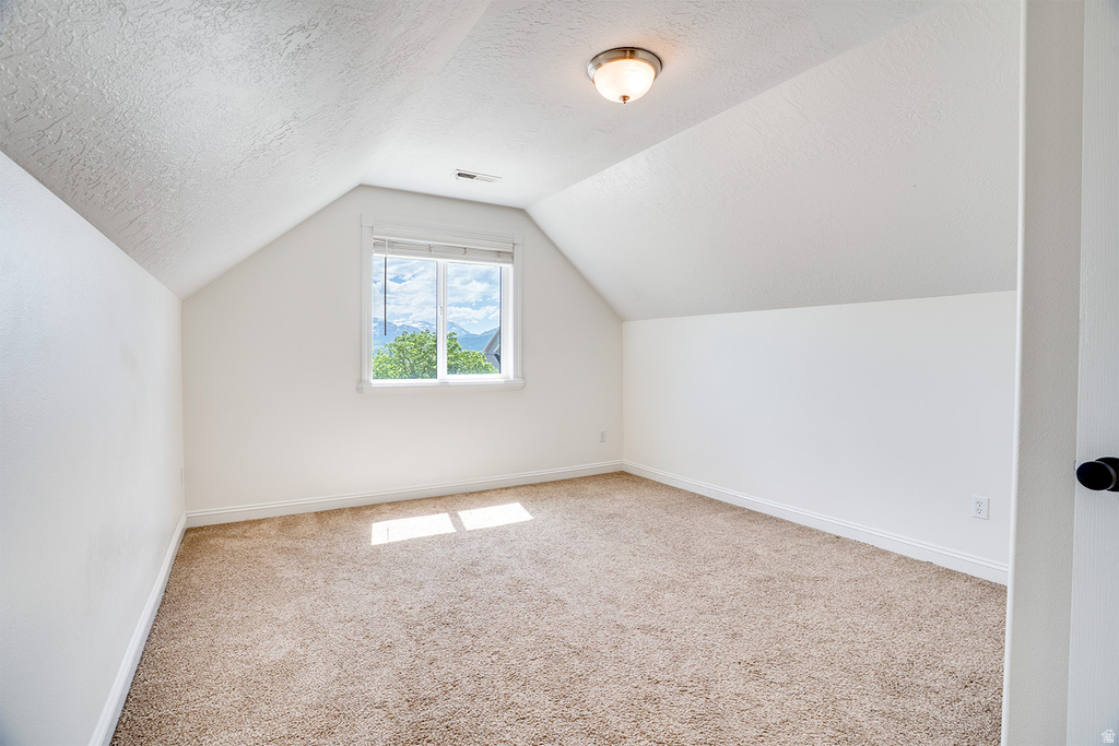 Attic room featuring a single window with mountain scenery, sloped ceilings, textured white walls, and light-colored carpet flooring