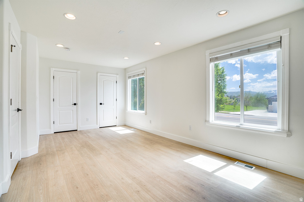 Bright room featuring wood-finish flooring, two white panel doors with black hardware, and recessed lighting