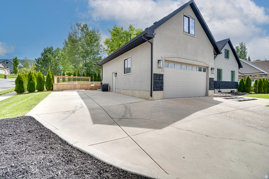 Stucco exterior with a pitched roof, attached garage, extended concrete driveway, and a wood deck with railings