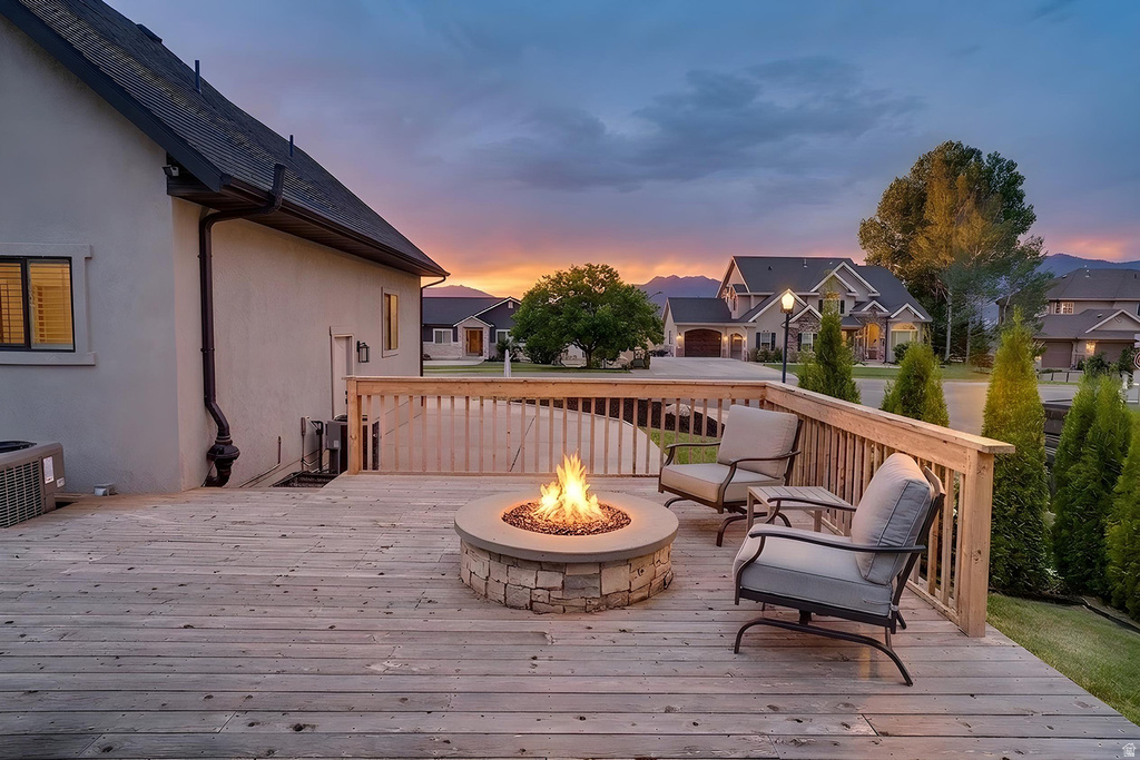 Expansive wood-finish deck with a stone fire pit, wood railing, and surrounding greenery