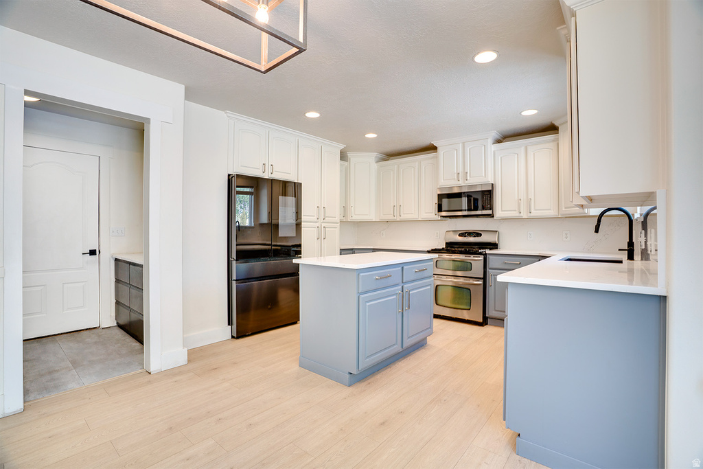 Modern kitchen featuring light wood-finish flooring, white upper cabinetry, and contrasting blue-gray lower cabinetry