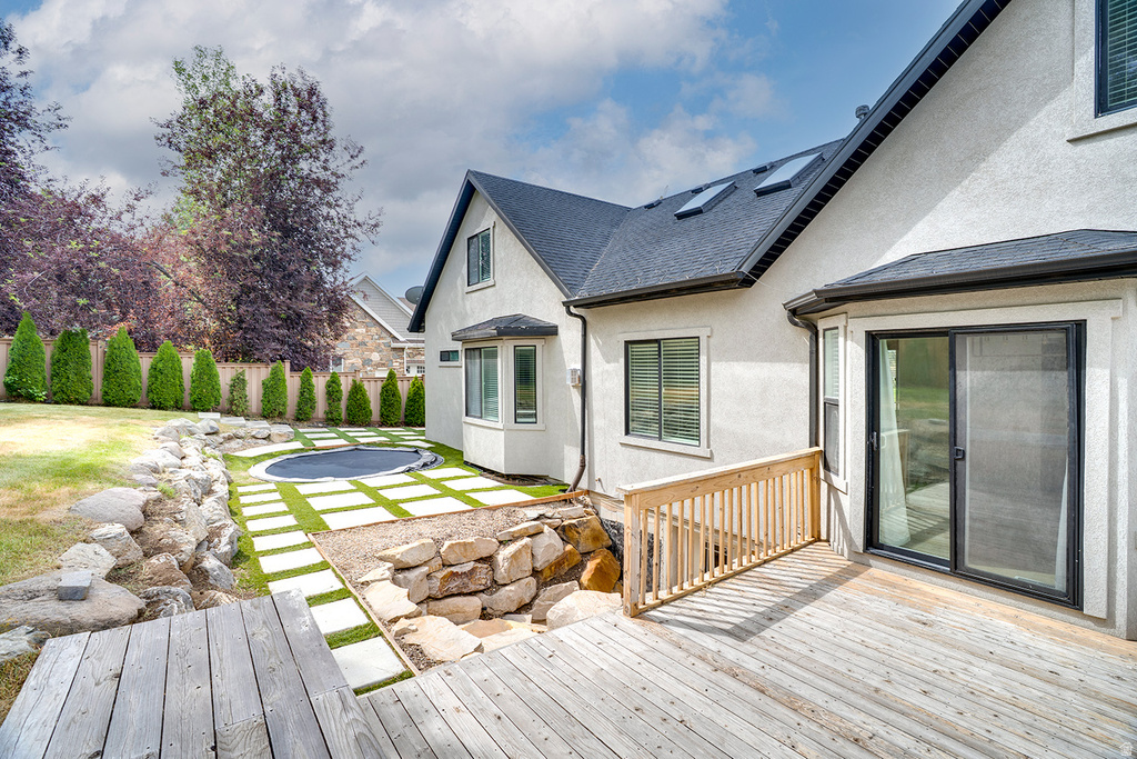 Spacious backyard featuring a wood deck, integrated trampoline, and a terraced rock garden
