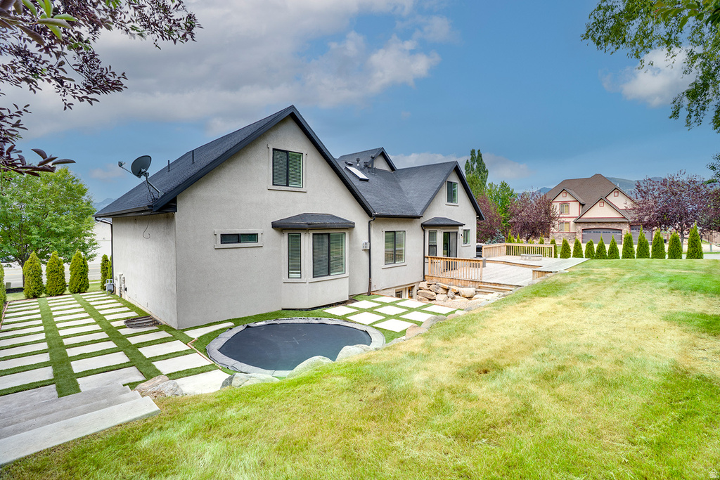 Rear exterior showcasing a multi-level wood deck, a sunken trampoline feature, and a patterned paver pathway