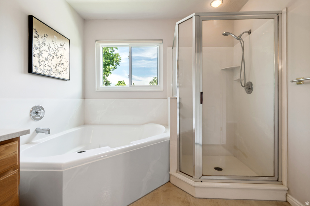 Spacious bathroom featuring a corner soaking tub, a separate glass-enclosed shower, a large window, light wood-finish cabinetry, and neutral-toned wall paint