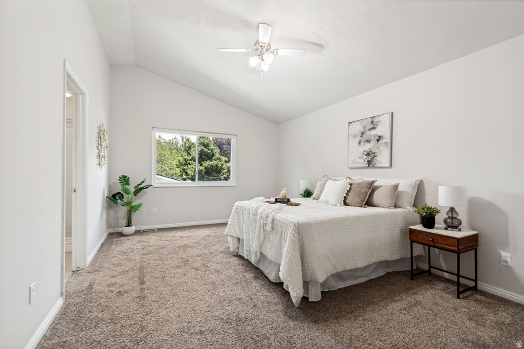 Vaulted ceiling bedroom with a window overlooking mature trees, neutral-toned carpet, and a ceiling fan with integrated lighting