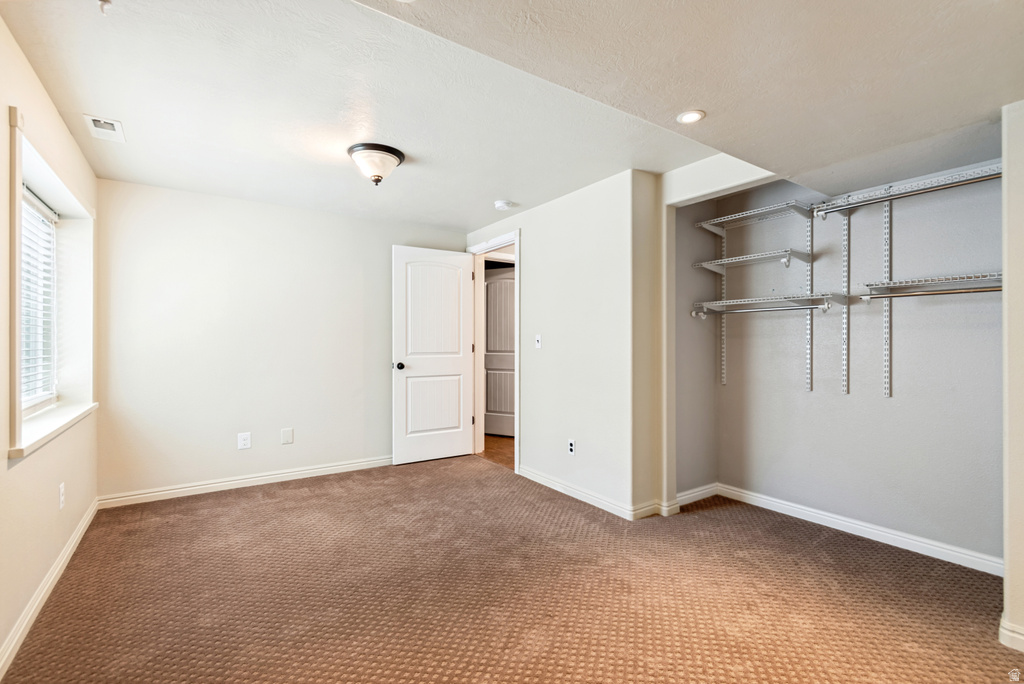 Carpeted room featuring a window with blinds, a white paneled door, a ceiling-mounted light fixture, recessed lighting, and an open closet with adjustable shelving and hanging rods
