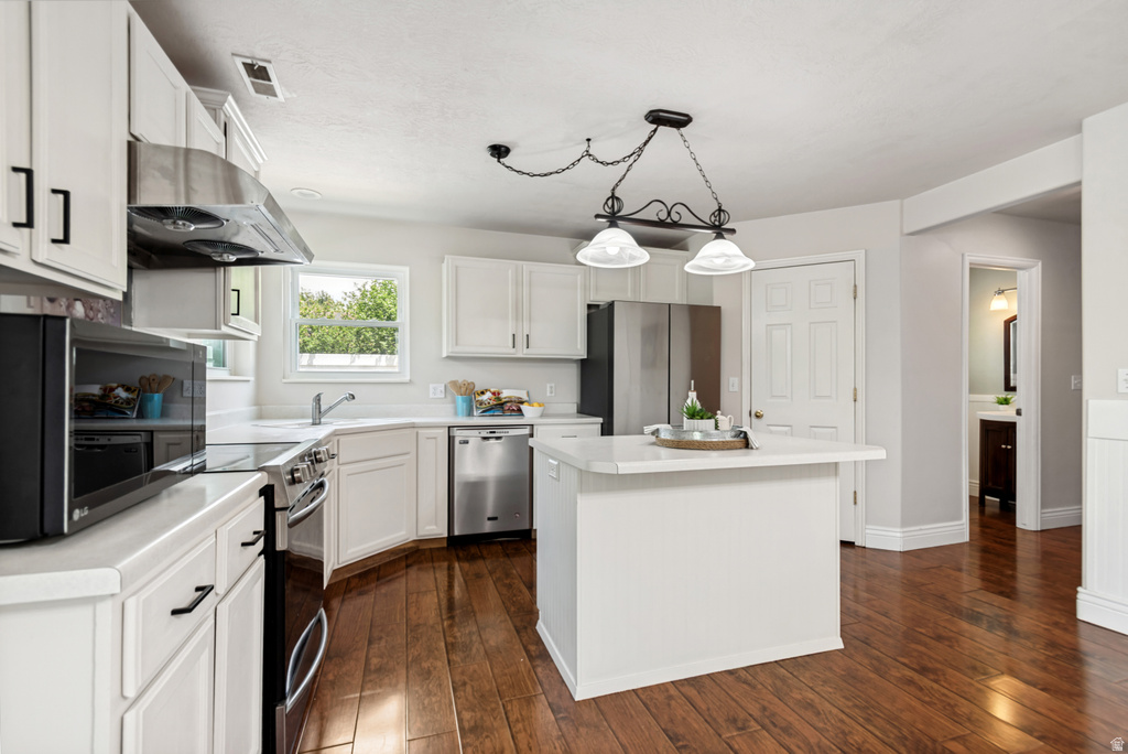 Kitchen featuring white cabinetry, wood-finish flooring, stainless steel appliances, a center island with a light-colored countertop, and a double-window