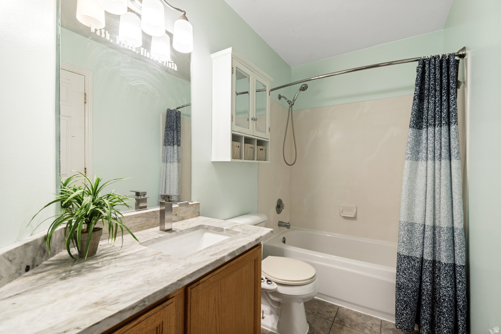 Bathroom featuring a single vanity with a stone-finish countertop and integrated sink, a large wall-mounted mirror, a built-in wall cabinet with glass-front doors, a shower-over-tub combination with a chrome showerhead, and tile flooring