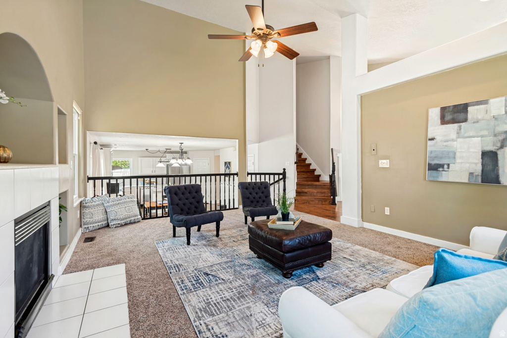 Vaulted ceiling living area featuring a ceiling fan, fireplace with white tile hearth, and a wood-finish staircase