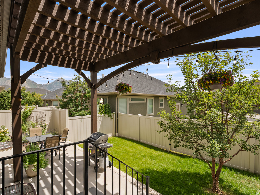 Expansive outdoor patio featuring a wooden pergola, string lighting, and a black metal railing