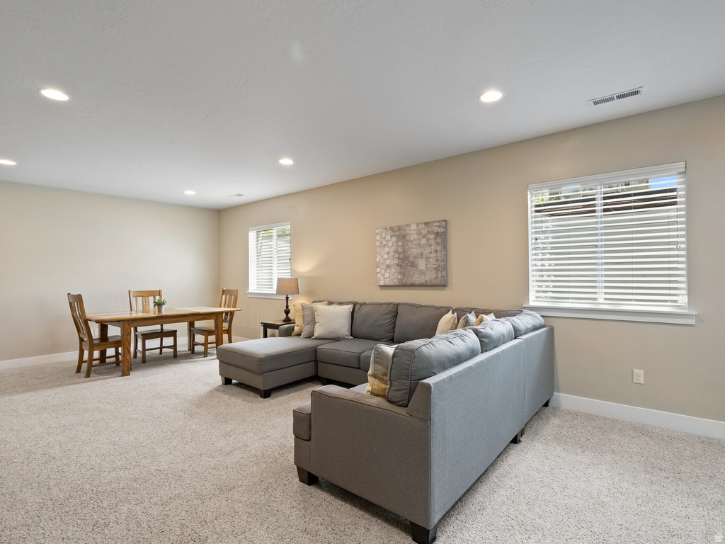Spacious living area featuring neutral-toned walls, recessed lighting, two windows with blinds, and light-colored carpeting