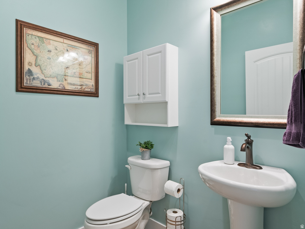 Bathroom featuring a pedestal sink with bronze-finish faucet, an elongated toilet, and a wall-mounted cabinet
