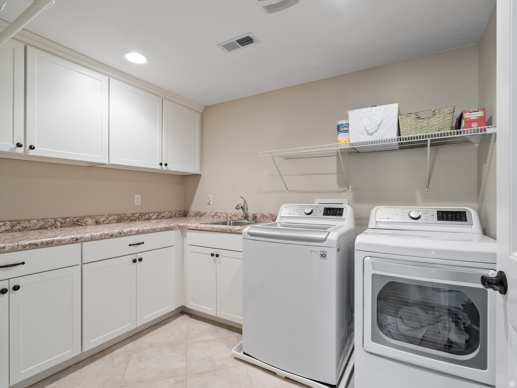 Laundry area featuring white cabinetry with black hardware, a stainless steel sink, and stone-finish countertops