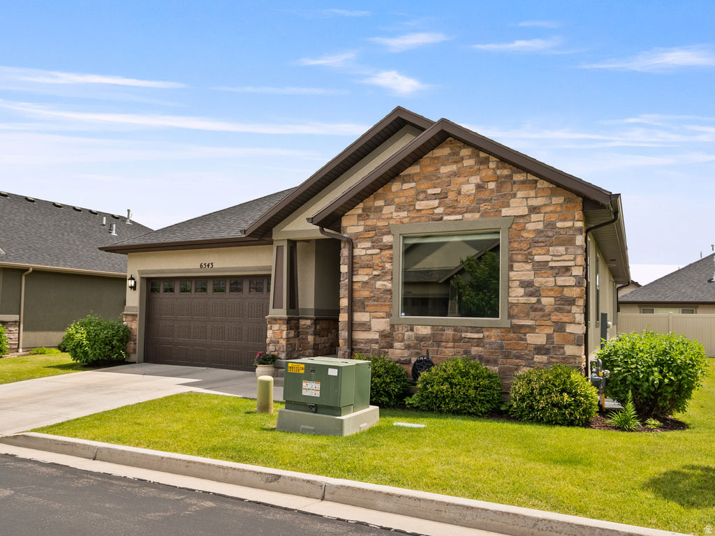 Stone and stucco exterior featuring a two-car garage, concrete driveway, and front lawn