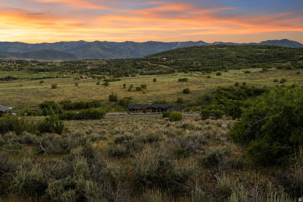 Expansive landscape featuring distant mountains, rolling hills, and a prominent residence with a dark roof and stone accents