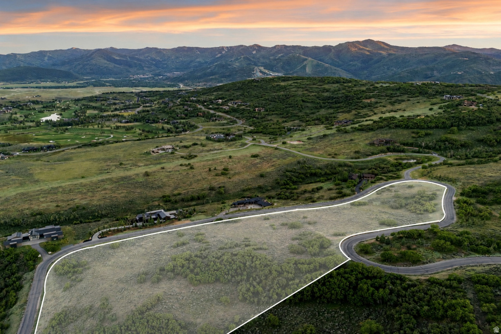 Expansive land parcel featuring a winding paved road, surrounding lush greenery, and distant mountain ranges