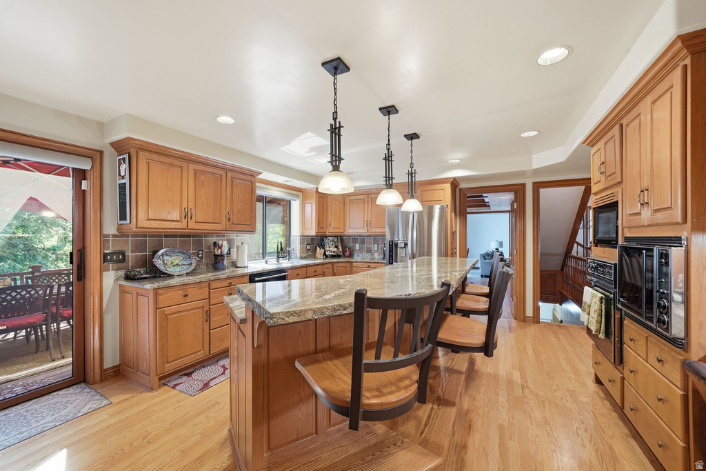 Kitchen featuring wood cabinetry, stone countertops, stainless steel appliances, a center island with pendant lighting, and wood-finish flooring