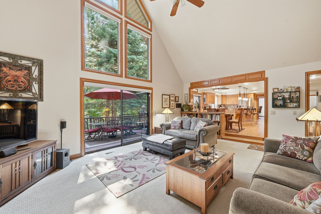 Vaulted living area featuring high ceilings, a wall of wood-framed windows, carpet flooring, and direct access to an outdoor deck