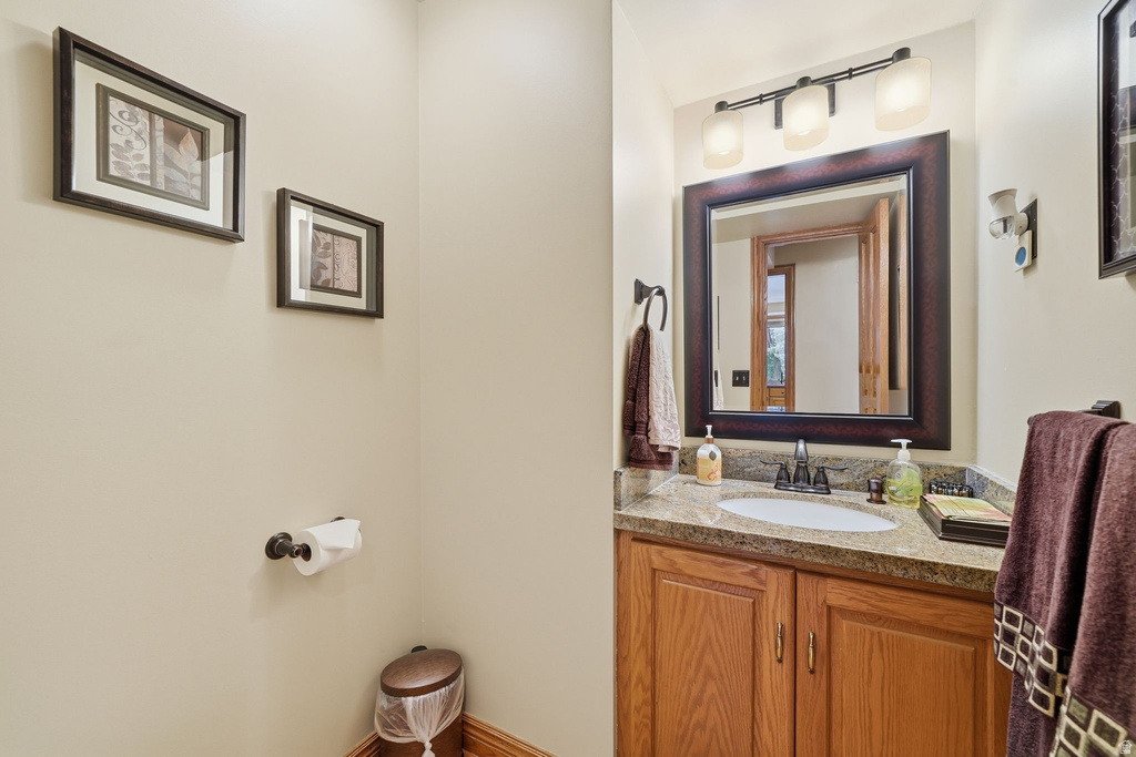 Vanity with integrated sink, stone-finish countertop, wood cabinetry, and framed mirror with three-bulb vanity lighting