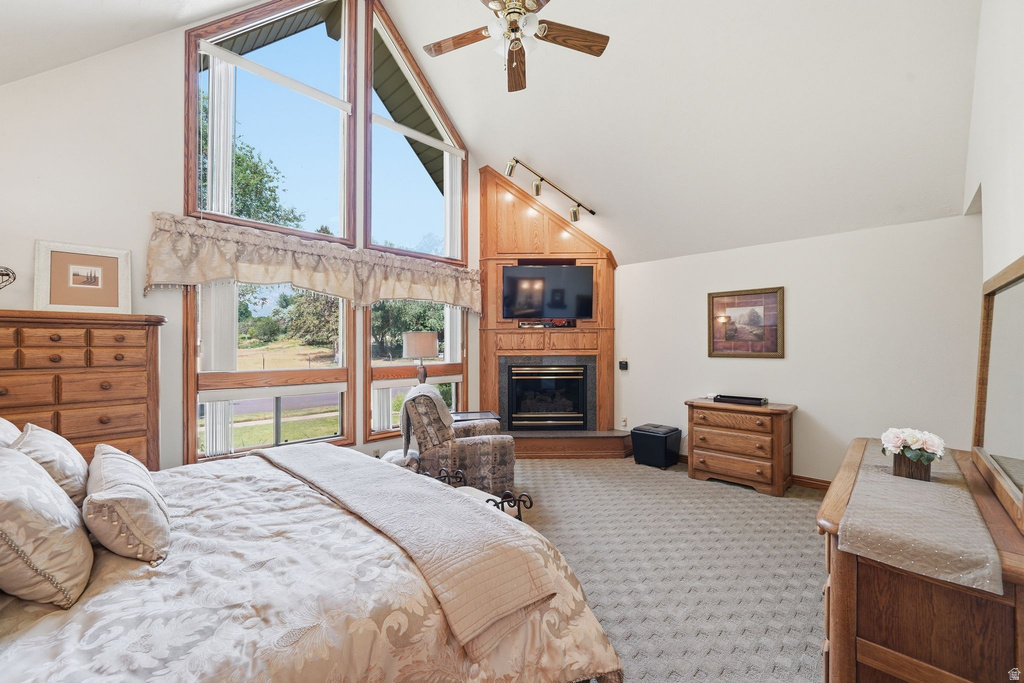 Vaulted ceiling bedroom featuring expansive windows, a wood-finish fireplace surround, and a ceiling fan