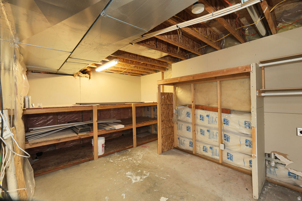 Unfinished basement space featuring exposed ceiling joists, concrete flooring, built-in shelving, and framed wall sections