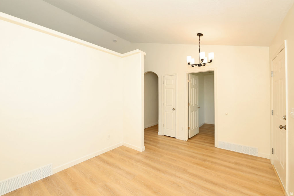 Open-concept living area with wood-finish flooring, a contemporary chandelier, vaulted ceiling, and arched entryway