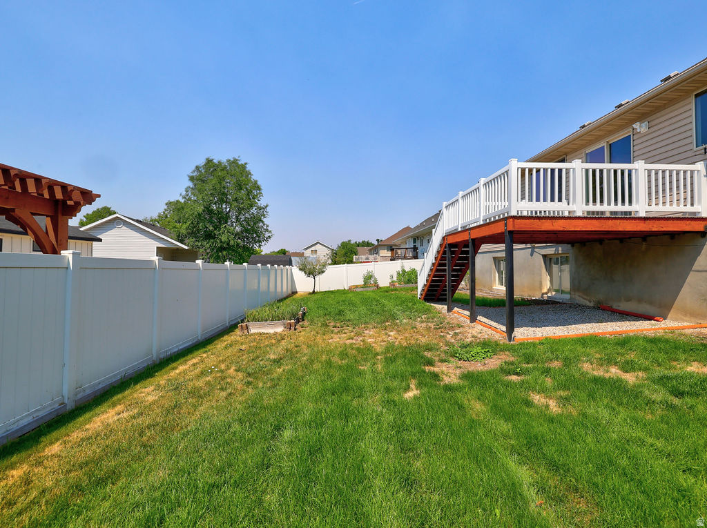 Expansive backyard featuring a white vinyl fence, a raised wood deck with white railings, and a gravel patio area under the deck