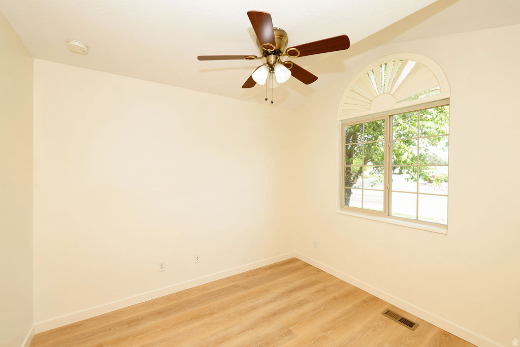 Room featuring a large arched window with a sunburst design, wood-finish flooring, a ceiling fan with integrated lighting, and neutral wall tones