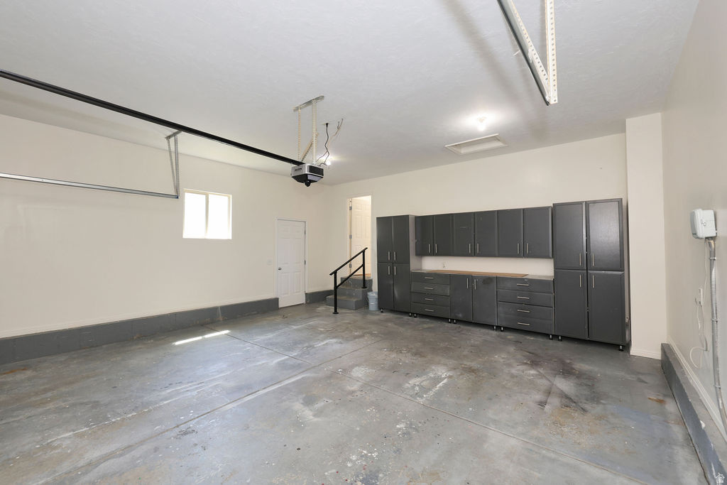 Spacious garage featuring extensive built-in gray cabinetry with wood-finish countertops, concrete flooring, and a single window for natural light