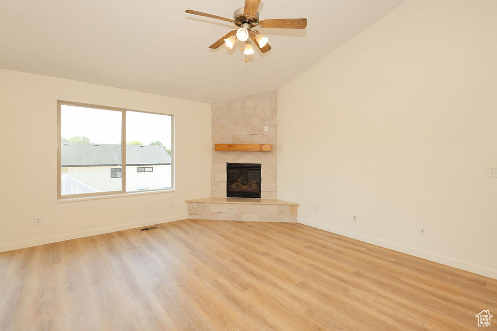 Vaulted ceiling great room featuring wood-finish flooring, a corner fireplace with a stone surround, and a natural wood mantel