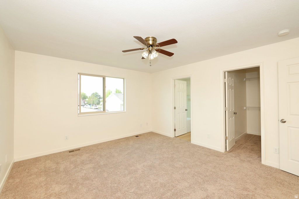 Spacious room featuring neutral carpet, a large window, and a ceiling fan with light fixture