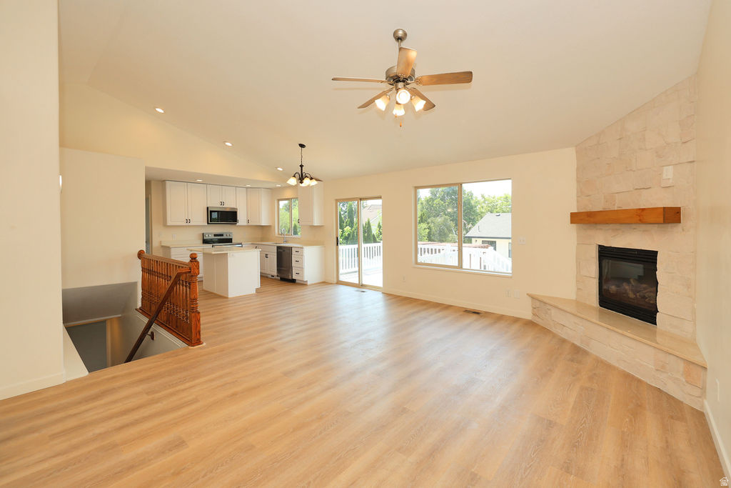 Spacious room featuring wood-finish flooring, a contemporary fireplace with a stone surround and wood mantel, white kitchen cabinetry with a central island, and a sliding glass door opening to an outdoor deck