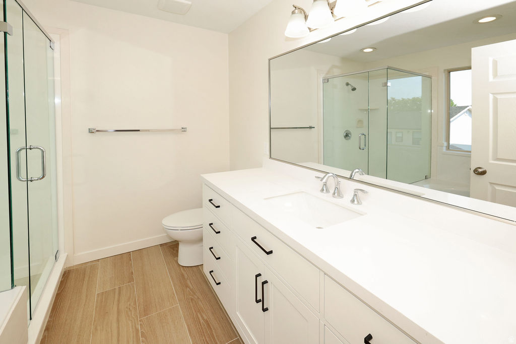Spacious bathroom featuring a double vanity with white cabinetry, light countertops, and wood-finish tile flooring
