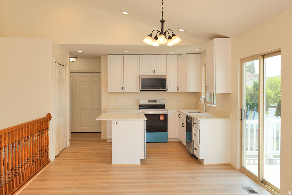 Open-concept kitchen featuring white cabinetry, stainless steel appliances, a center island with countertop seating, wood-finish flooring, and a sliding glass door to an outdoor area