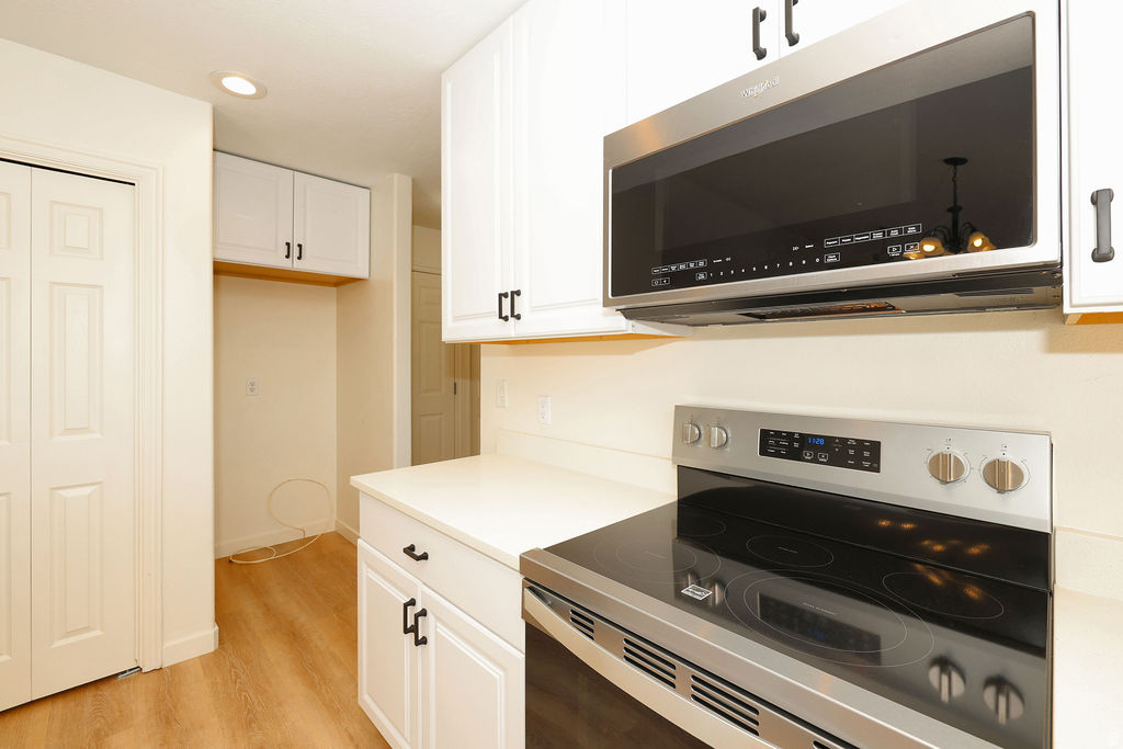 Kitchen featuring white cabinetry with dark hardware, a stainless steel over-the-range microwave, a stainless steel electric range with a black cooktop, and light-toned countertops