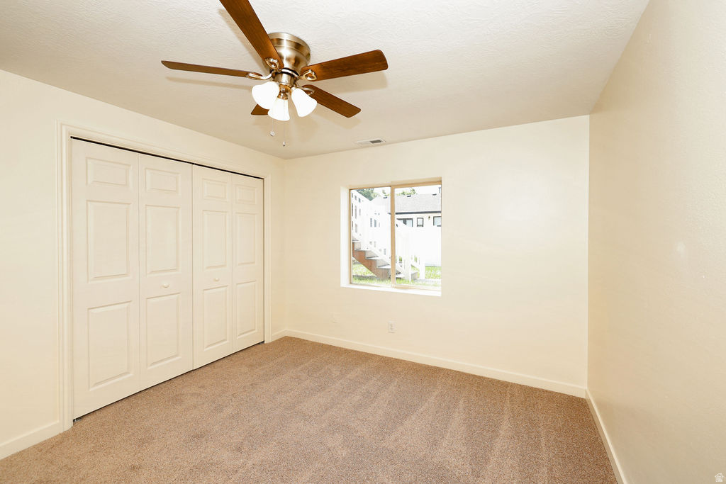 Bedroom featuring neutral-toned carpet, a four-panel bi-fold closet, and a ceiling fan with integrated lighting