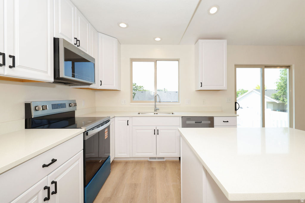 Modern kitchen featuring white cabinetry, light-toned countertops, stainless steel appliances, wood-finish flooring, and a sliding glass door