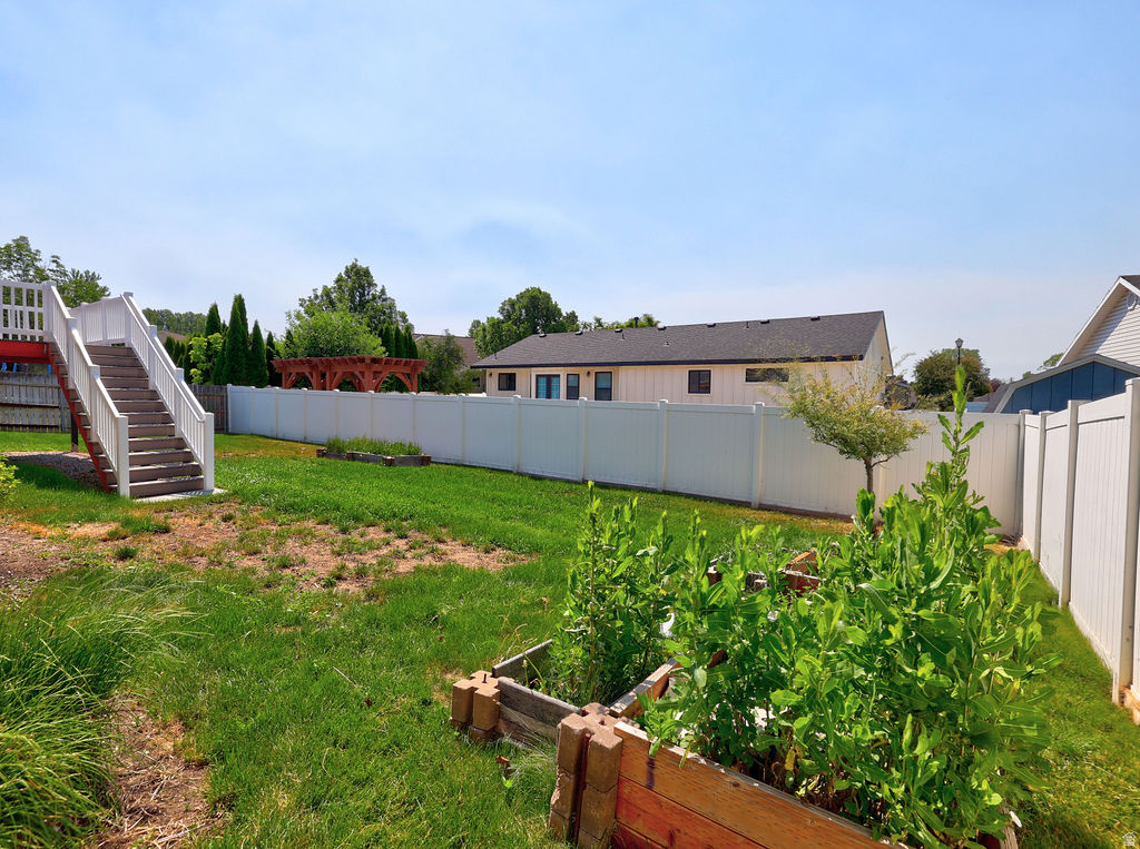 Spacious backyard featuring a white vinyl privacy fence, a wooden deck with white railings, and multiple raised garden beds
