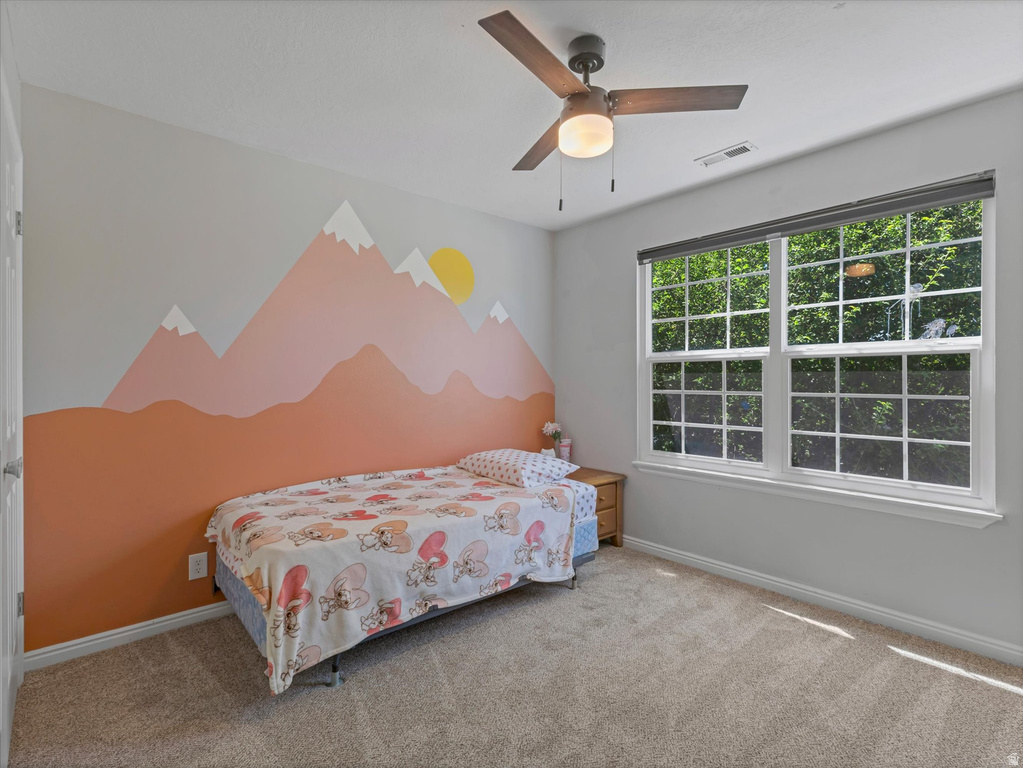 Bedroom featuring a decorative mountain mural wall, a large multi-pane window, and a ceiling fan with integrated lighting
