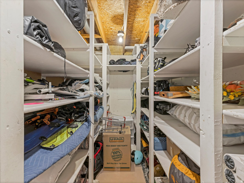 Dedicated storage room featuring multiple tiers of built-in shelving, exposed ceiling joists, and overhead lighting