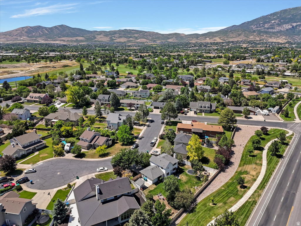 Expansive aerial showcasing a residential neighborhood with mature trees, mountain backdrop, and golf course access