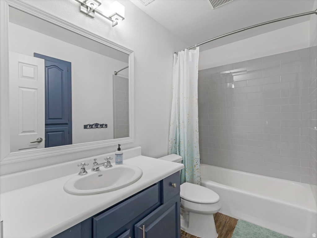 Bathroom featuring a wood-finish floor, white vanity countertop, built-in vanity with blue cabinetry, oval undermount sink, and a shower-over-tub with gray subway tile surround