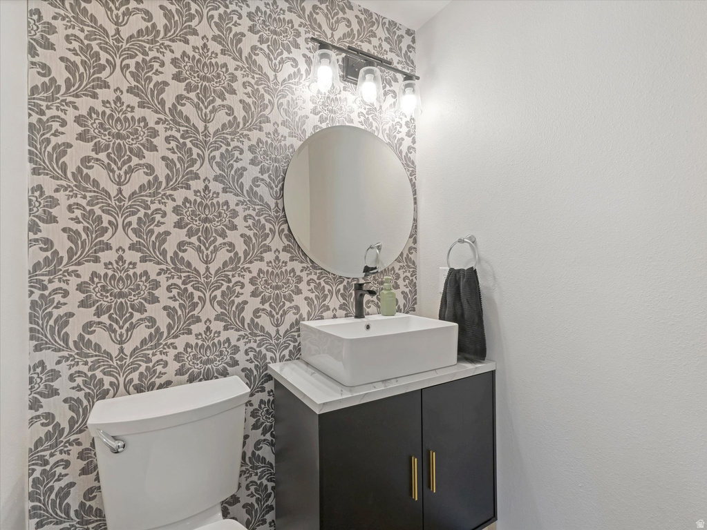 Powder room featuring a decorative accent wall, rectangular vessel sink, black cabinet vanity with gold-tone hardware, and a circular mirror