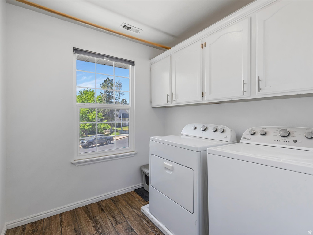 Laundry area featuring wood-finish flooring, white cabinetry with brushed nickel hardware, and a single window with natural light