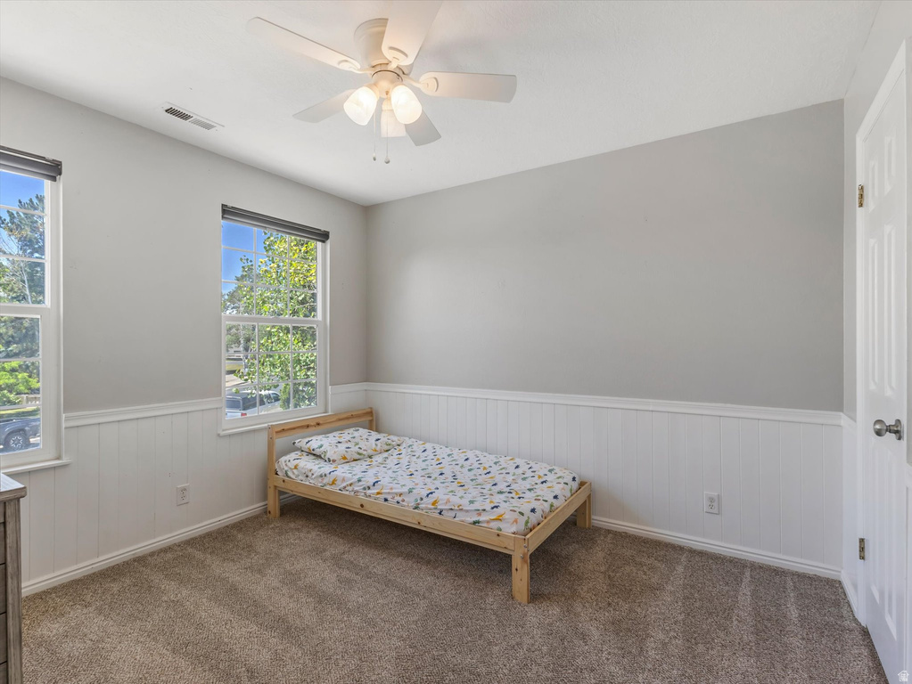 Interior room featuring two large windows, a ceiling fan with integrated lighting, wainscoting, and carpet flooring
