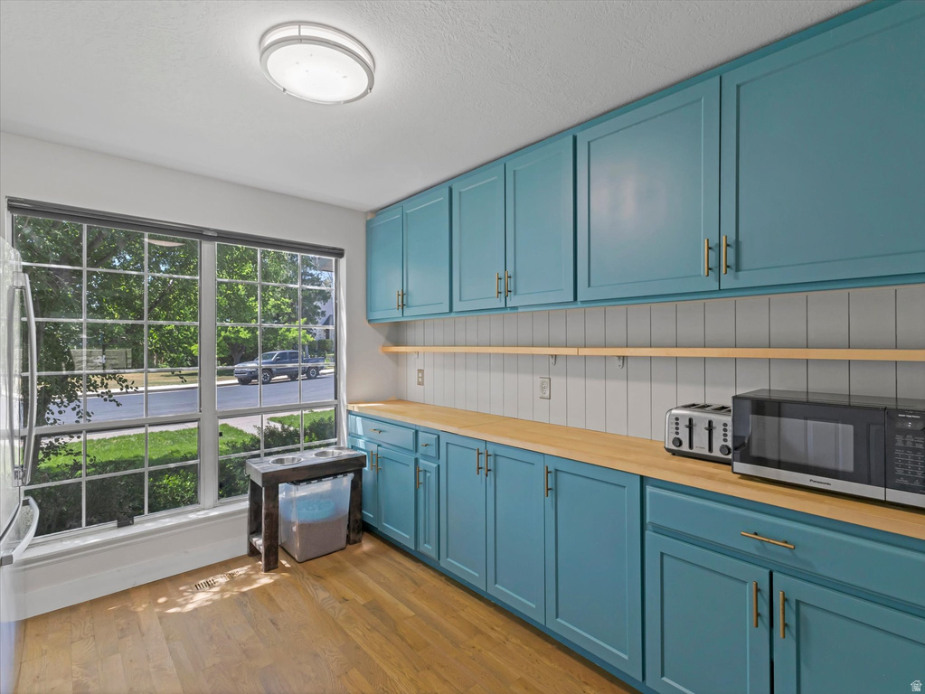 Kitchen featuring wood-finish flooring, a large multi-pane window, extensive blue cabinetry with gold-tone hardware, wood-finish countertops, and a white vertical shiplap backsplash