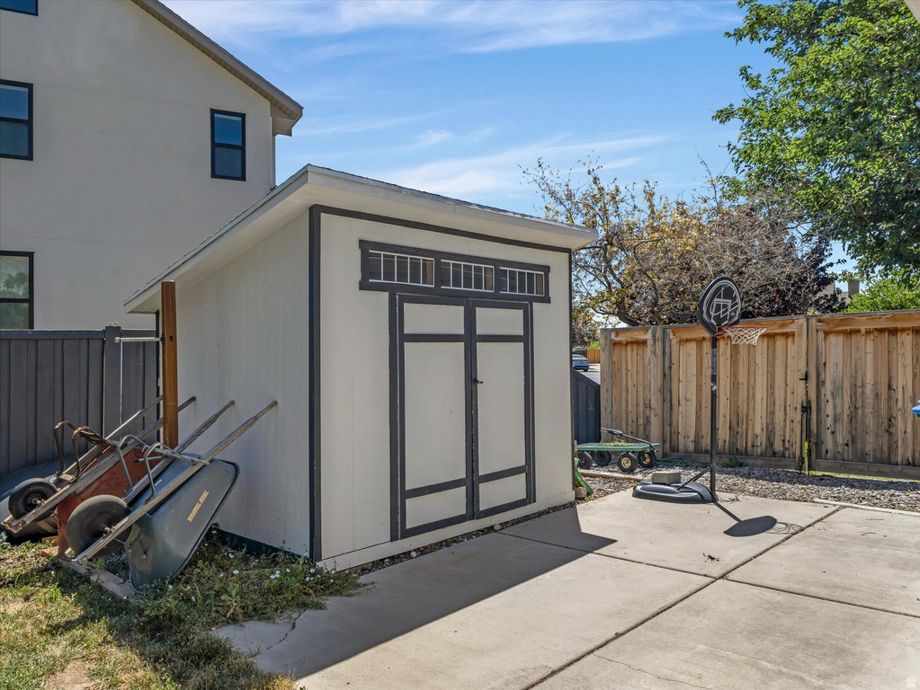 Backyard featuring a shed with a white exterior and dark trim, concrete patio, and natural wood privacy fencing