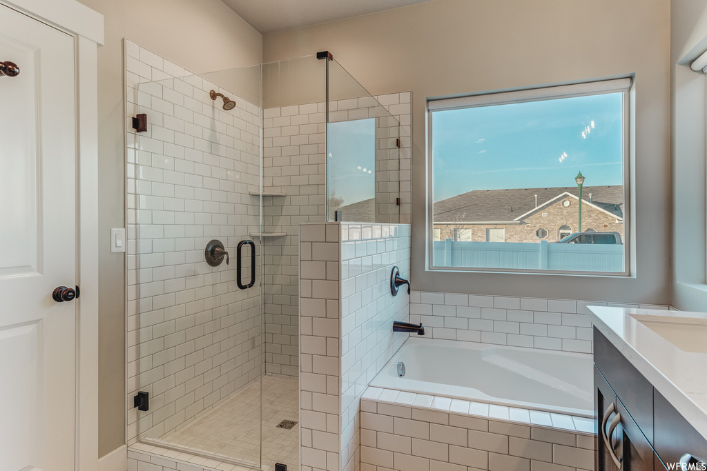 Spa-inspired primary bathroom featuring a frameless glass-enclosed walk-in shower with subway tile surround, a soaking tub positioned beneath a large window with natural light, dual vanity with quartz countertop, and matte black hardware and fixtures